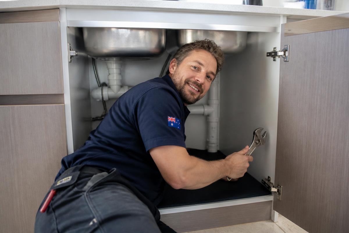 Australian plumber working under a kitchen sink